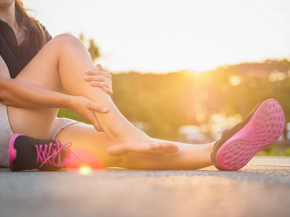 Runner seduta a terra al tramonto che si tiene la caviglia e il tallone per il dolore